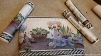 Photo showing four rolls of floral wallpaper borders partially unrolled with flower pot designs on carpeted floor.