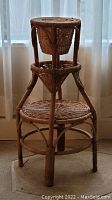 Full view of the wicker plant stand showing three tiers and woven wicker structure against a light curtain background.