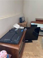 Two flat screen TVs shown in a basement setting; one 46-inch Vizio TV on top of a vintage TV stand, one 28-inch TV standing on the floor angled against a mirrored surface.