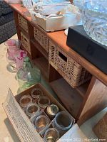 Photo showing wooden coffee table with woven baskets in cubbyholes and glass jars near base