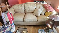 Full front view of the beige faux leather couch with pillows showing wear and stains