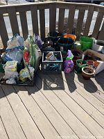 Full view of assorted gardening supplies on a wooden deck including varied pots, planters, soil, and fertilizer bags.