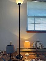 Photo showing four lamps against a wall and window. One tall floor lamp and three smaller tabletop lamps, including a Tiffany style.