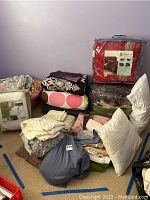 Photo showing a pile of bedding items including comforters, folded sheets, pillows, and mattress pad