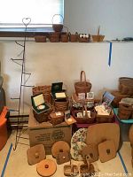 Wide view of assorted Longaberger baskets, some with lids, ceramic ornaments in boxes, gift tags, and the metal heart hanging rack visible on left side.