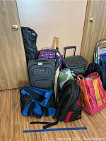 Photo of assorted luggage and bags including rolling suitcases, backpacks, cooler bag, umbrellas, tote bag, and stadium chair.