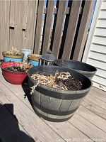 View of assorted garden planters on wooden deck with some containing soil and dried plants, and a black metal lantern visible