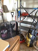 Power washer, wet dry vac, tools, fan, and extension cords shown together in corner with shelving unit