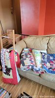 Photo showing three folded quilts and a pillow cover draped over a wooden ladder next to a beige couch.