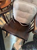 Top-down view of the wooden rocking chair seat showing dark wood surface with some scratches and a beige tie-on padded seat cushion.