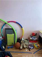 Photo of various sporting goods, toys, board games, and roller skates on floor against a wall