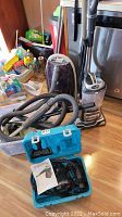 Three vacuums shown together in a kitchen including Shark Navigator, Kenmore Progressive, and blue Turbosteamer in carrying case, with hoses and accessories