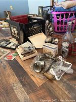 Photo showing vintage photos and albums in a crate, vintage metal meat grinder parts, bear figurine, tin recipe box, and empty Jack Daniel's bottle along with flasks