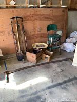 Full lot showing tree cutting saw, sled, crates, stool, broom, and other items against plywood wall.