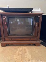 Full front view of the vintage Magnavox TV housed in a wood cabinet on a hardwood floor, showing the screen and wood frame.