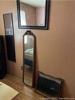 Four decorative wall mirrors leaning against a beige wall showing varying frame styles and sizes with visible frame chipping and one broken piece