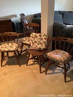 Four wooden chairs with seat cushions, three Longaberger floral cushions and one Mary Englebreit patterned cushion, medium brown wood, visible scratches and wear.