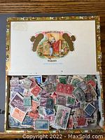 Open Romeo y Julieta Habana cigar box filled with assorted used postage stamps showing front side with colorful stamp designs and postmarks