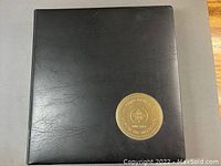 Front cover of black coin album holder showing gold embossed round logo with maple leaf and text.