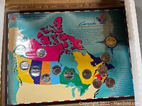 Full view of coin set displayed on colorful map of Canada in original packaging with coins mounted on display board.