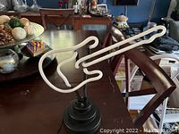 Guitar-shaped white neon light mounted on tiered black base shown from the front and side angles.