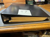 Black three-ring binder containing stamp collection viewed from the side showing thickness