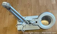 Side view of white magnifying desk lamp showing adjustable arm, clamp base, and cable wrapped around arm.