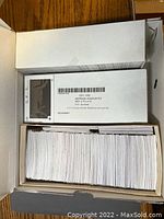 Box of white cardboard stamp display cards with black plastic windows stacked inside, label visible on top card box showing quantity 1,000 and product details.