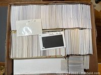 Box with several thousand white stamp catalog cards stacked inside, some cards visible at the top showing catalog price details.