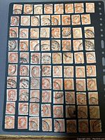 Grid of 80 Small Queens Canada postage stamps all used with cancellation marks, orange color, arranged on black album page.
