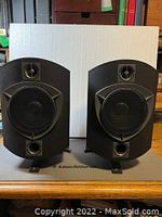 Front view of pair of black B&W Rock Solid speakers on stands showing woofer, tweeter and port