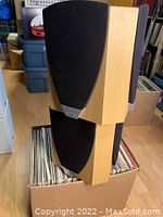 Pair of Jamo surround speakers stacked on vinyl records showing wood finish and black grill cover.