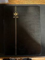 Black Uni-Safe branded stock book closed, showing cover with gold vertical stripes and logo.