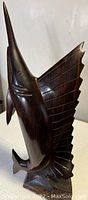 Full view of sailfish wooden carving showing upright pose with large dorsal fin and smooth polished surface.