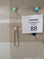 Photo of 14k gold bracelet hanging on a beige carpet under pastel colored push pins with auction lot paper nearby