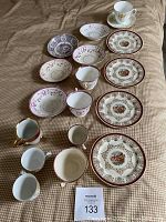 Group of 18 antique and vintage china pieces including plates, saucers and teacups with floral and scenic designs.