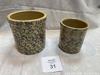 Pair of Robinson Ransbottom spongeware crocks side by side on a neutral background with a MaxSold lot number card in front