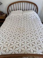 White crocheted blanket laid on a bed, showing full surface with geometric star-like crochet pattern.
