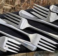Close-up view of multiple salad forks showing detailed Queen Anne pattern of handles and mix of glossy and satin finish.