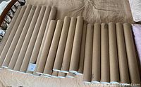 Group of 24 mailing poster tubes laid on a bed, showing the full set composition with visible white plastic end caps and brown cardboard body.