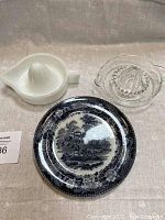 Photo of the three items: one black and white decorative plate, one white milk glass juicer, one clear glass juicer.
