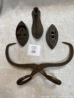 Top-down image of four cast iron items on light cloth: two sad irons, one large ice tong, one cobbler's tool.