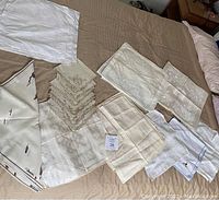 Various folded and stacked vintage cotton, linen, and damask napkins in shades of white, beige, and cream laid out on a bedspread.