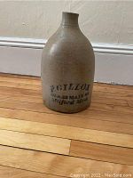 Full view of stoneware jug on wooden floor, showing overall shape, color, and advertising text on front.