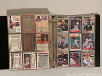 Open 3-ring binder showing double-sided pages of sports trading cards including baseball and basketball players. Cards displayed in plastic sleeves with backs visible on left, fronts on right.