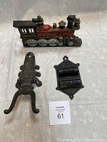 All three cast iron items displayed together on fabric background: boot jack, train doorstop, match holder