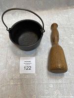 Cast iron handled bowl next to wooden pestle on a flat surface.