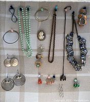 Top view of assorted costume jewelry laid out on beige plaid fabric including necklaces, rings, earrings, and brooches as described