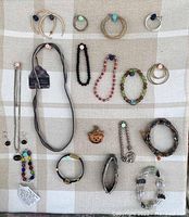 Overview of multiple costume jewelry pieces including necklaces, bracelets, and several pairs of earrings laid out on a cloth.