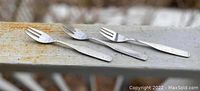 Three identical stainless steel forks with three prongs placed on a weathered wooden surface, showing their design and size.